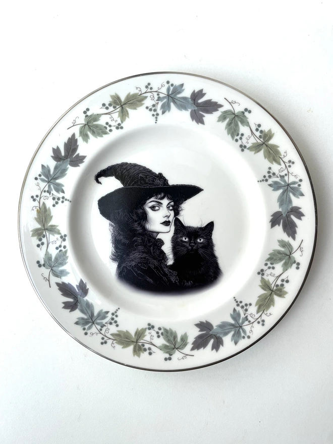 vintage plate with an ornate border, with a printed vintage illustration of a Victorian witch and her black cat in the middle