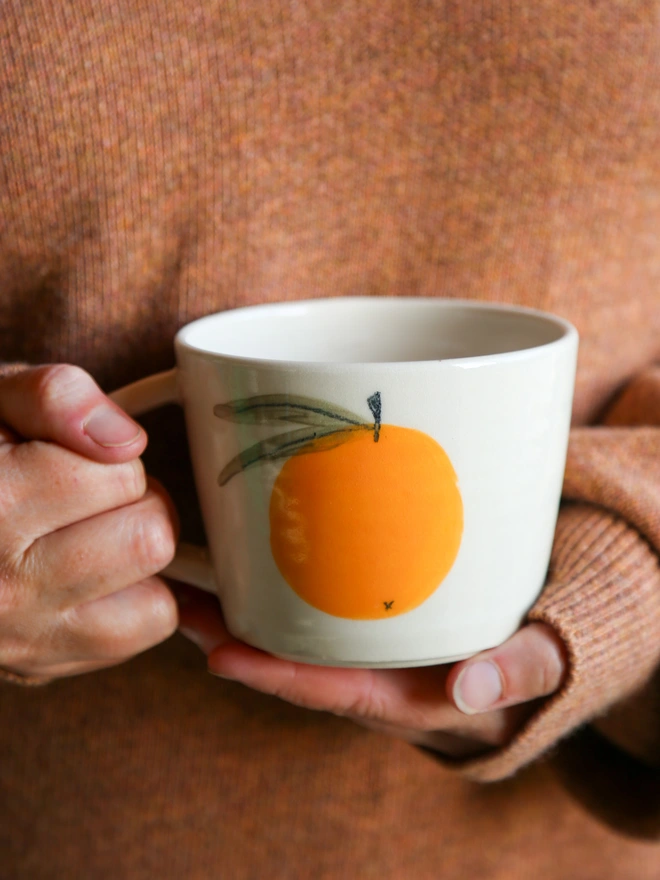 HOLDING A STONEWARE MUG WITH BOLD CLEMENTINE DESIGN