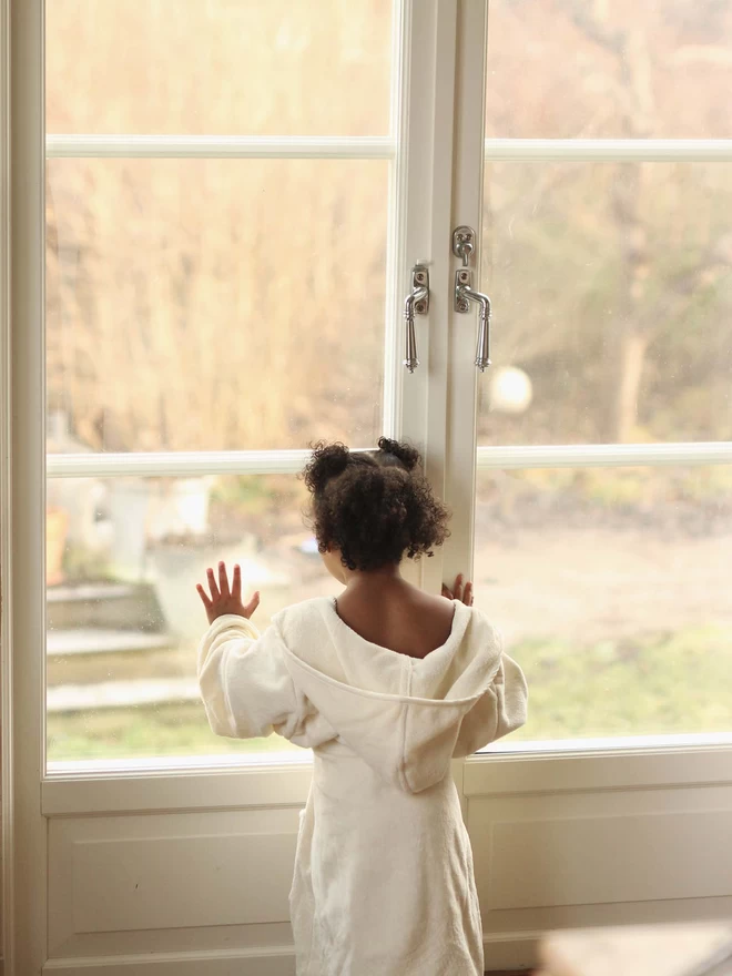 A girl wearing a towelling robe looking outside the window