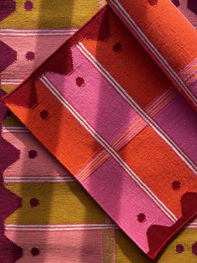 Ladder Flatweave Runner Rug, one rolled pink and orange runner sitting atop a pink and yellow runner.