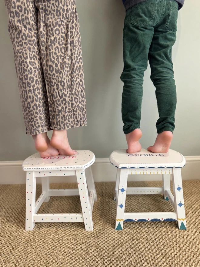 Two children standing on hand painted stools. 