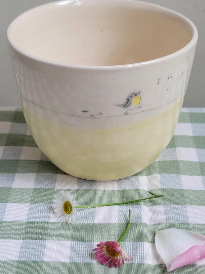 a yellow ceramic tumbler cup with a yellow robin song bird walking around the side with bird prints and whistled musical notes