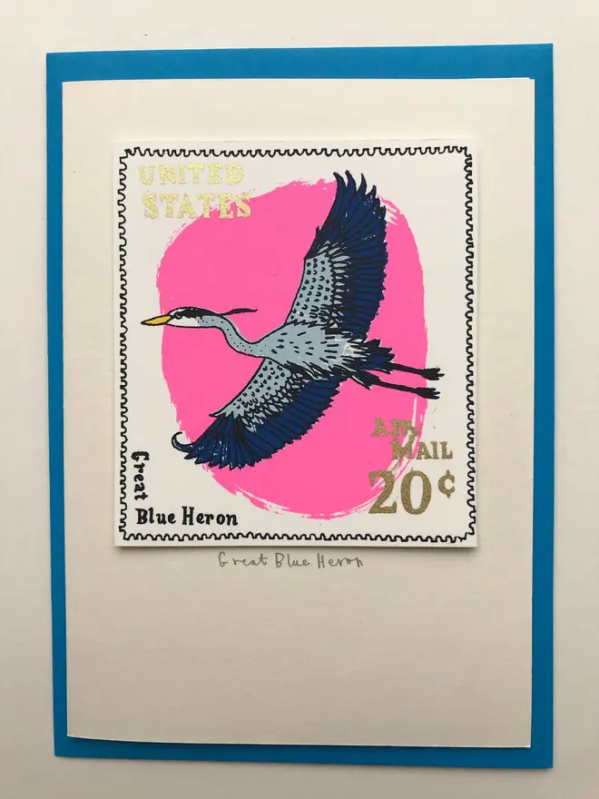 Bird Stamp Card Great Blue Heron/ American, a white card with a colourful bird design in the centre against a blue envelope on a white surface. 