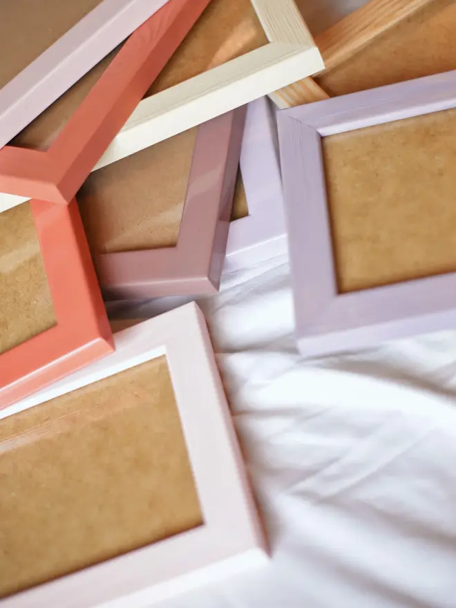 pile of various coloured empty flat wood picture frames on a white bed