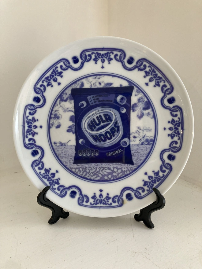 Blue and white Delft style decorative plate featuring a packet of Hula Hoops crisps in the centre.