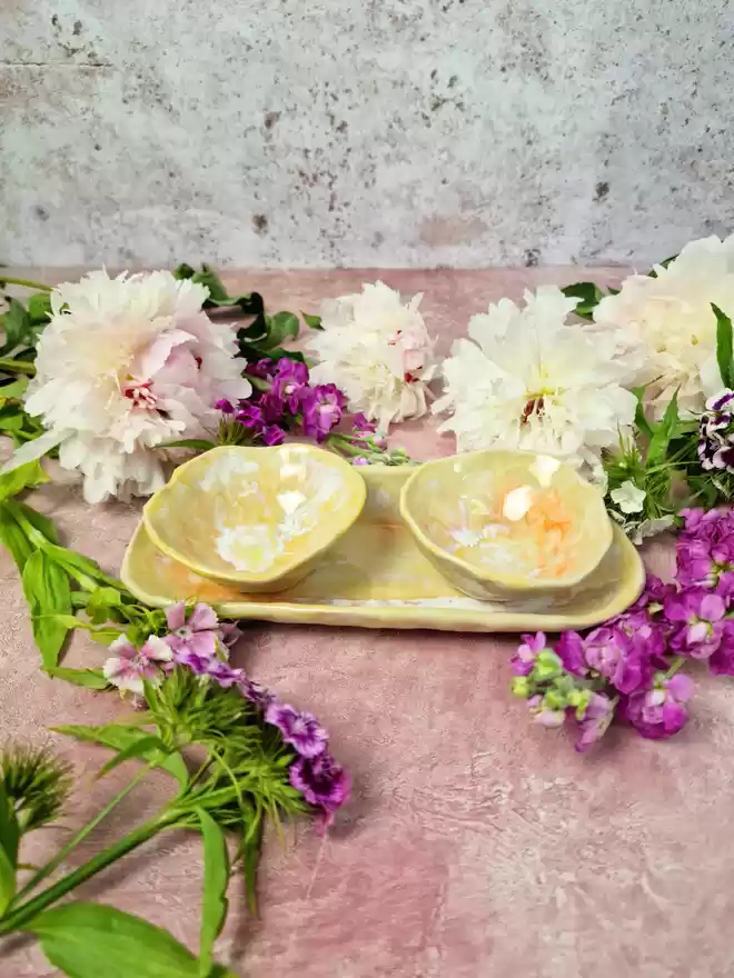 Serveware, Small serving dish crafted from stoneware clay and glazed in Ochre Yellow with yellow tones, creams, whites, hints of orange. Two bowls and an oval dish, tapas dish, snack dish, gift, handmade, homeware, pink background, flowers