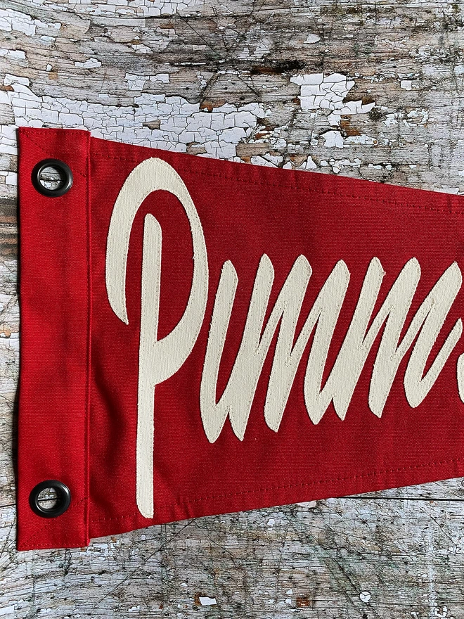 A Close up section of a red canvas Pimm's O Clock pennant. You can see ivory lettering.