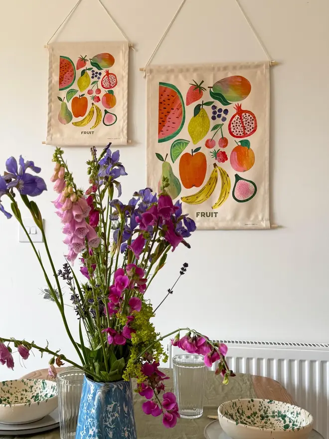 Fruit Print Fabric Banner, hanging on a white wall, next to a set table with flowers. 