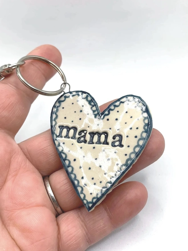 Mama Heart Ceramic Keyring, a person holding a blue keyring above a plain white surface. 