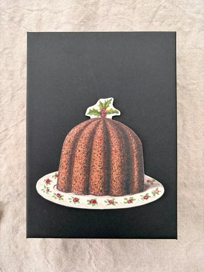 A slim black box with a Victorian Christmas pudding on it.