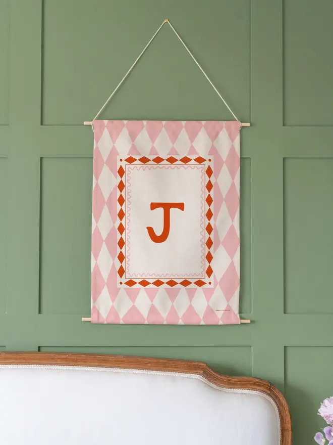 Harlequin Initial Fabric Banner, pink mini and midi next to each other against a green wall. 