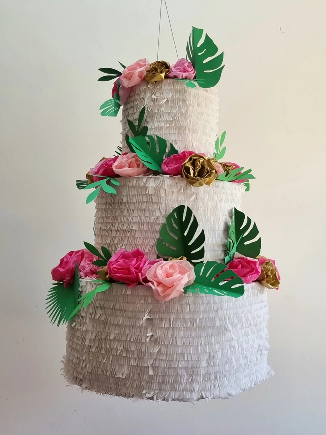 3 tier wedding cake pinata with a tropical theme. pink flowers and tropical leaves top every tier