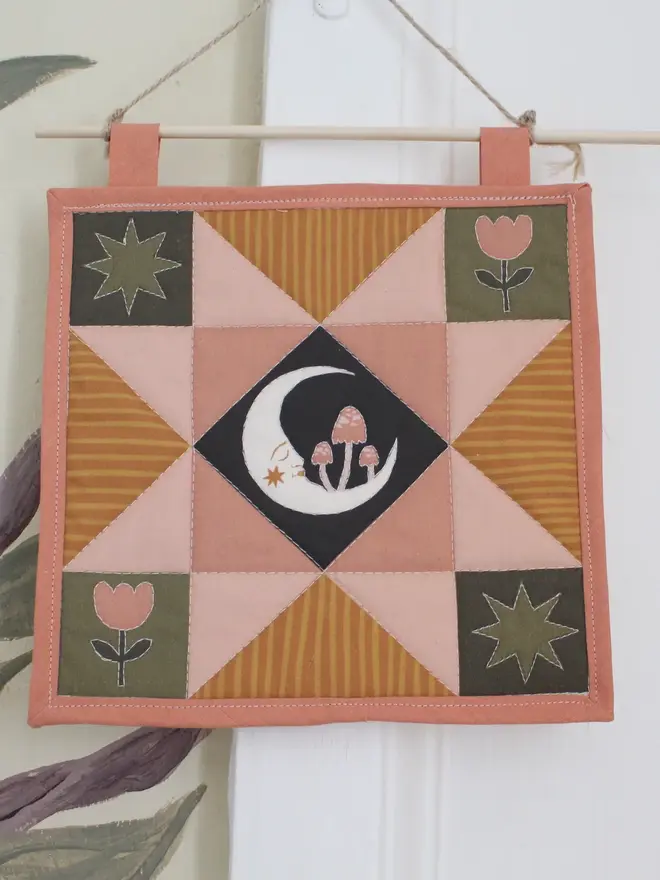 moon folk art quilt hanging. a patchwork hanging quilt with an embroidered moon in the centre.