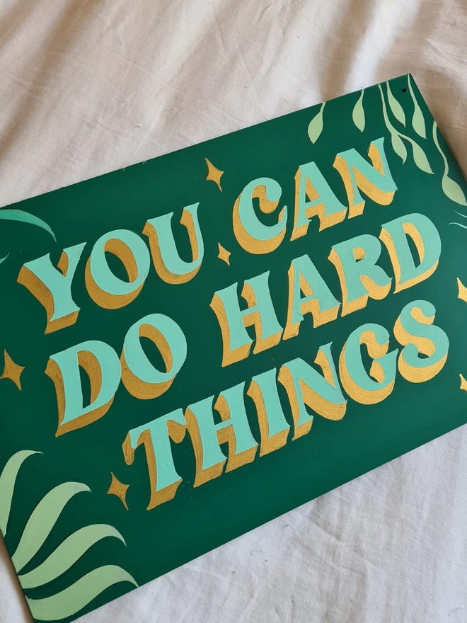 'You Can Do Hard Things' hand-painted onto a green panel with pale green lettering, metallic gold close shade and floral details.