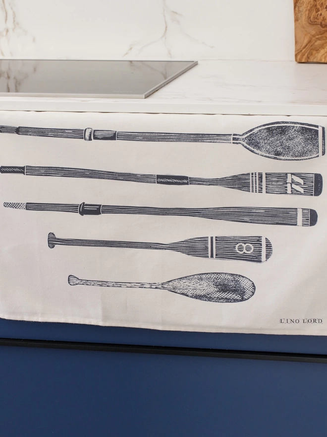 Picture of a tea towel in a kitchen with an image of oars and paddles, taken from an original lino print