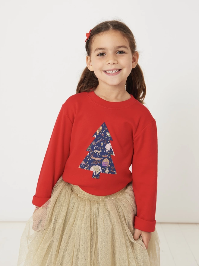 smiling girl wearing a red t-shirt with a Liberty Christmas print tree on the front