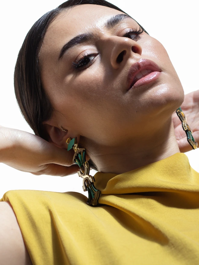 A person wearing a gold and green earring with a blurred background