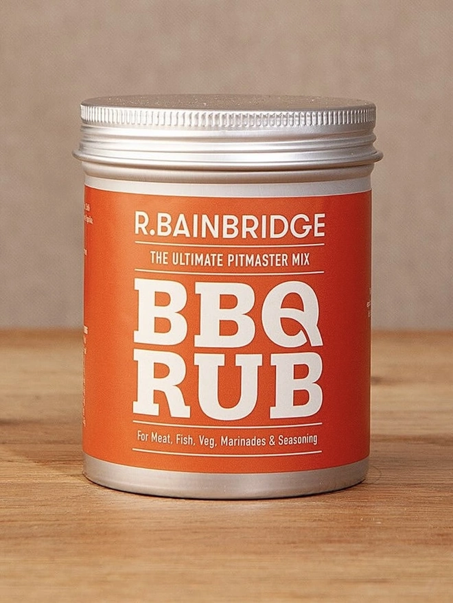 BBQ Rub Seasoning, a jar of seasoning sitting on a wooden surface against a plain backdrop. 