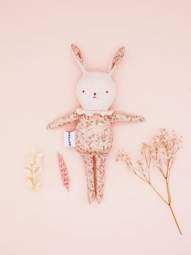 A handmade fabric doll in pastel floral prints, designed with distinct rabbit features. This doll has a linen face, simple embroidered features, and delicate ruffled collars, showcasing their artisan craftsmanship.