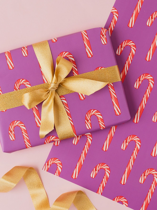 Purple Christmas wrapping paper featuring a repeating pattern of hand-drawn red and white striped candy canes.