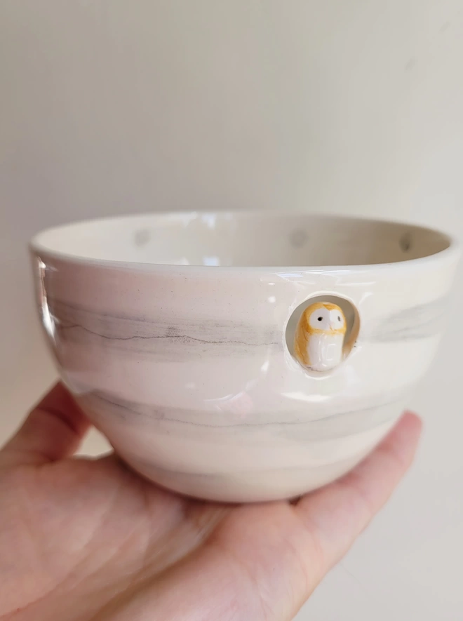  ceramic owl bowl held in a hand with a small barn owl perched in a cut out at the top front of the grey and white pottery dish