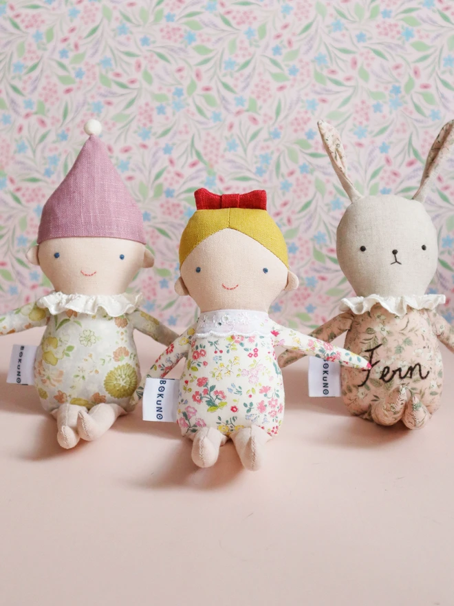 A handmade Spring Elf Doll with light skin, a soft pink floral print body, and a lavender-pink hat topped with a white pompom. The doll has a gentle smile and wears a ruffled white collar.