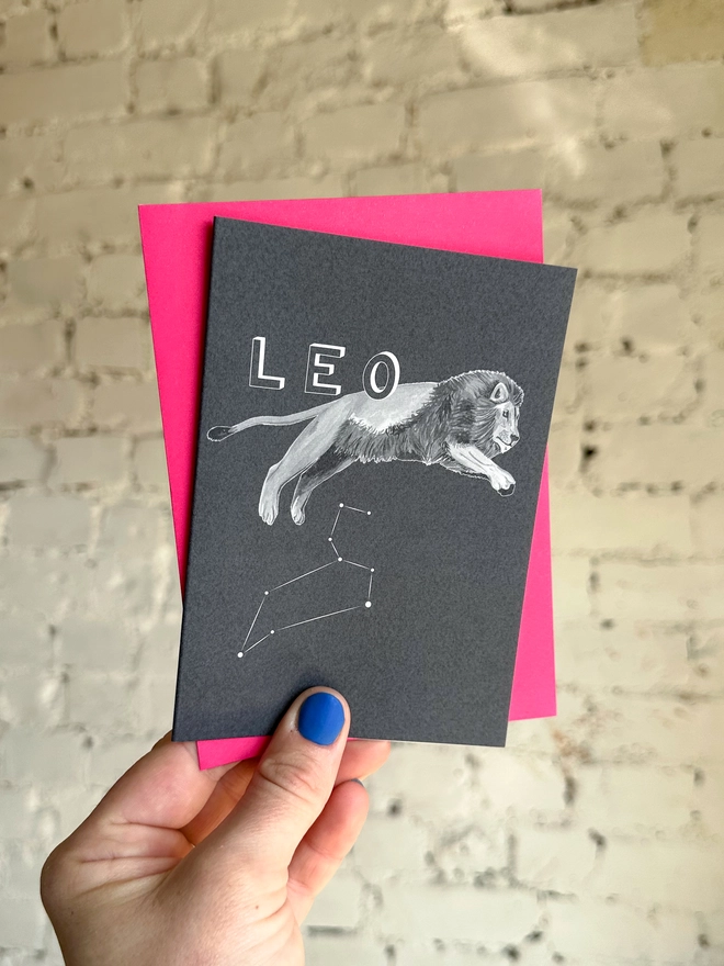 : a greetings card featuring a greyscale illustration of a zodiac style lion with the text “LEO” with a neon pink envelope