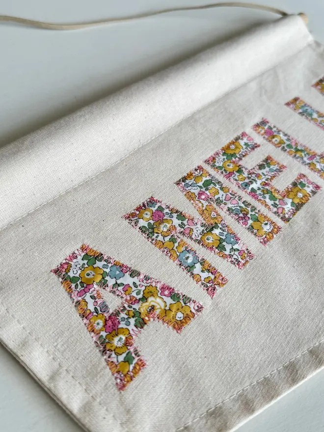 Personalised Name Banner. A banner with pin and yellow floral letter saying AMELIA