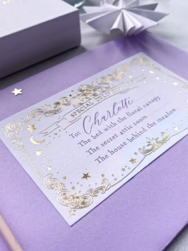 A gold foil "Special Delivery" label addressed to Charlotte, "the bed with the floral canopy," sits on a lilac envelope. A white gift box and paper star sit just behind.
