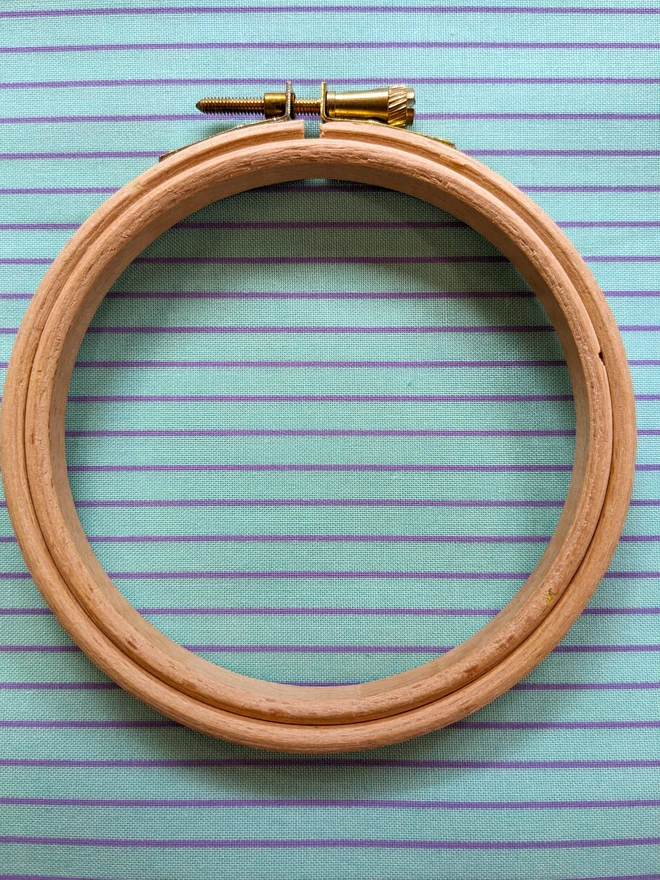 a wooden embroidery hoop lying on a stripy aqua coloured fabric