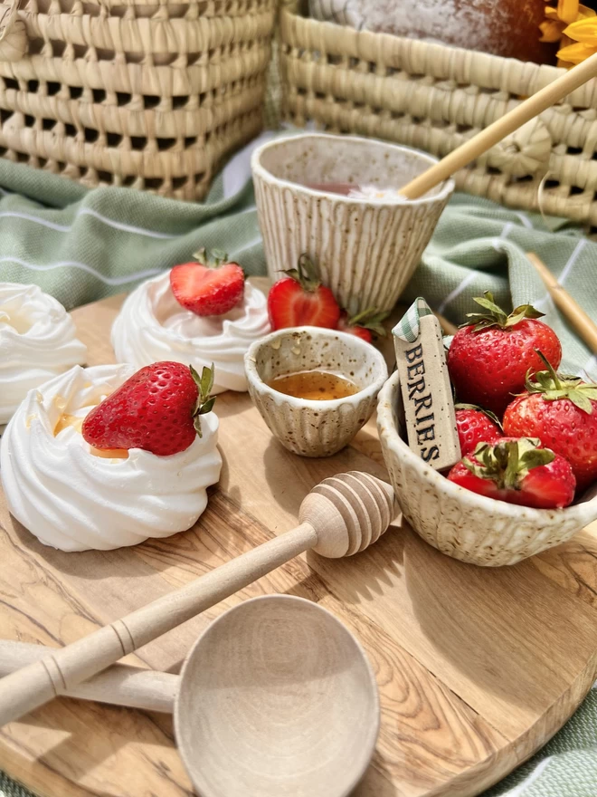 wooden board with a selection of ceramic pots holding strawberries, one pot also holds a ceramic tag with the word 'berries' embossed in black 