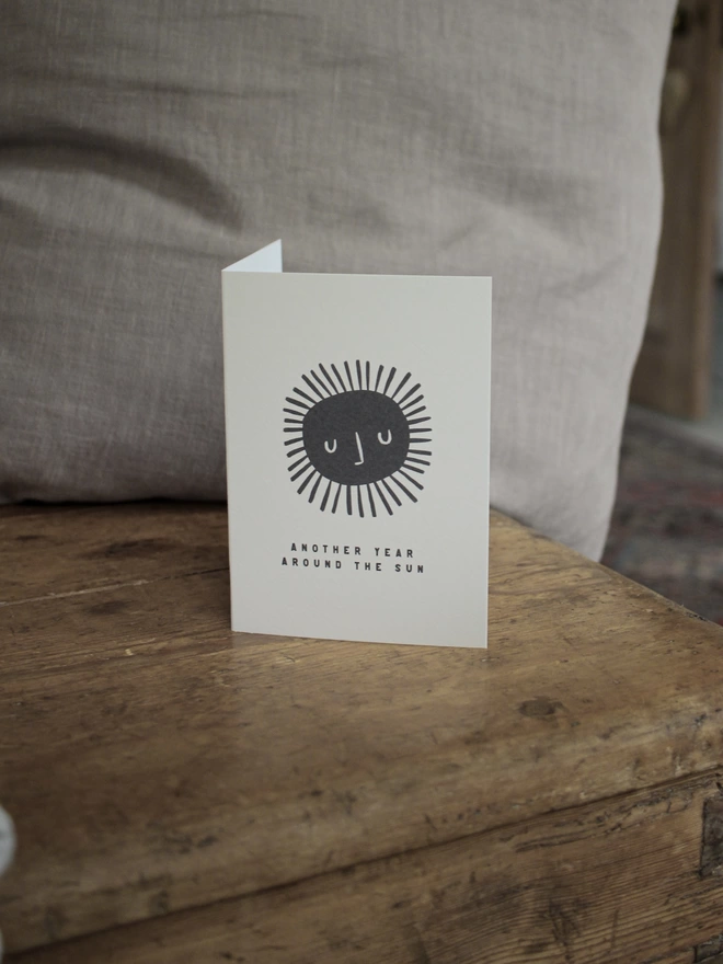 Black and white birthday card with illustration and the words Another year around the sun written on it stood up on wooden surface 