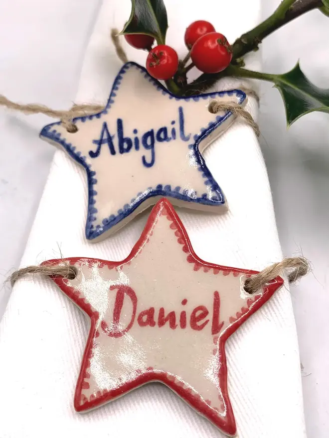 Personalised Ceramic Christmas Star Name Place Markers, a colourful ceramic start sitting on a white surface attached to a holly bush. 