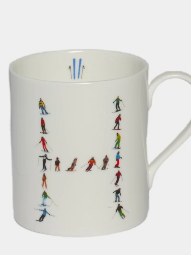 A simple white mug illustrated with an ‘H’ made of small, multicoloured skiers. The mug is set against a plain, white background.