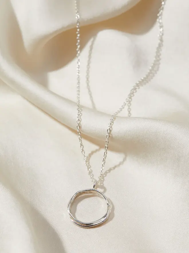 Dainty Sterling Silver Open Circle Necklace draped over silk material