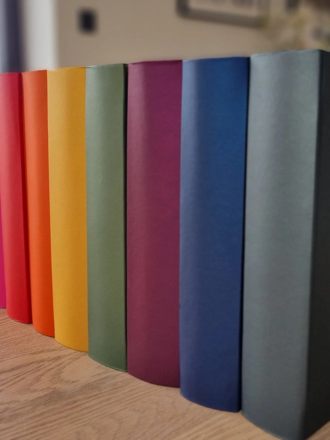 A row of brightly coloured photo albums are lined up on a wooden table top.