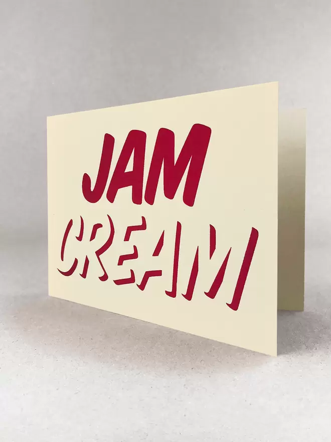 Cream at the bottom, Jam on top, printed in red ink on this cream card. Stood in a light grey studio with soft shadows.