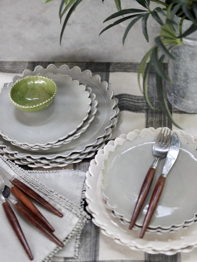 two stacks of daisy dinner plates with cutlery on a plaid cloth. Plates are grey and white with daisy side plates stacked on top