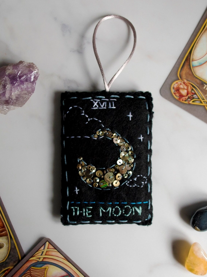 A handcrafted felt ornament with sequins and embroidery depicting "The Moon" tarot card. 