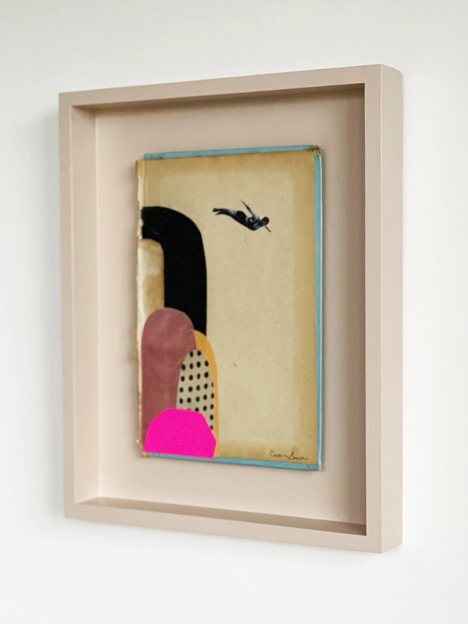 A diving portrait artwork on a vintage book cover, float mounted within a pale pink wood frame.
