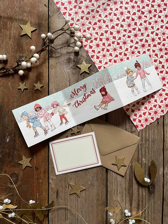 a concertinaed Christmas postcard featuring a vintage style illustration of children ice skating drawn in a vintage traditional story book style
