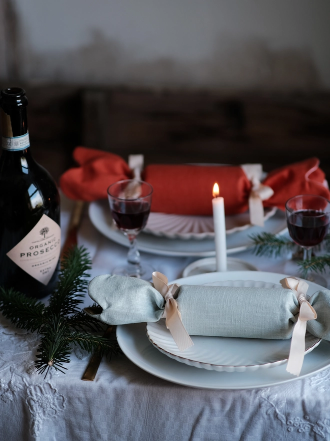 Reversible reusable linen Christmas crackers in soft pink, sage green, cream and muted festive colours, tied with natural ribbon and arranged on a family Christmas table