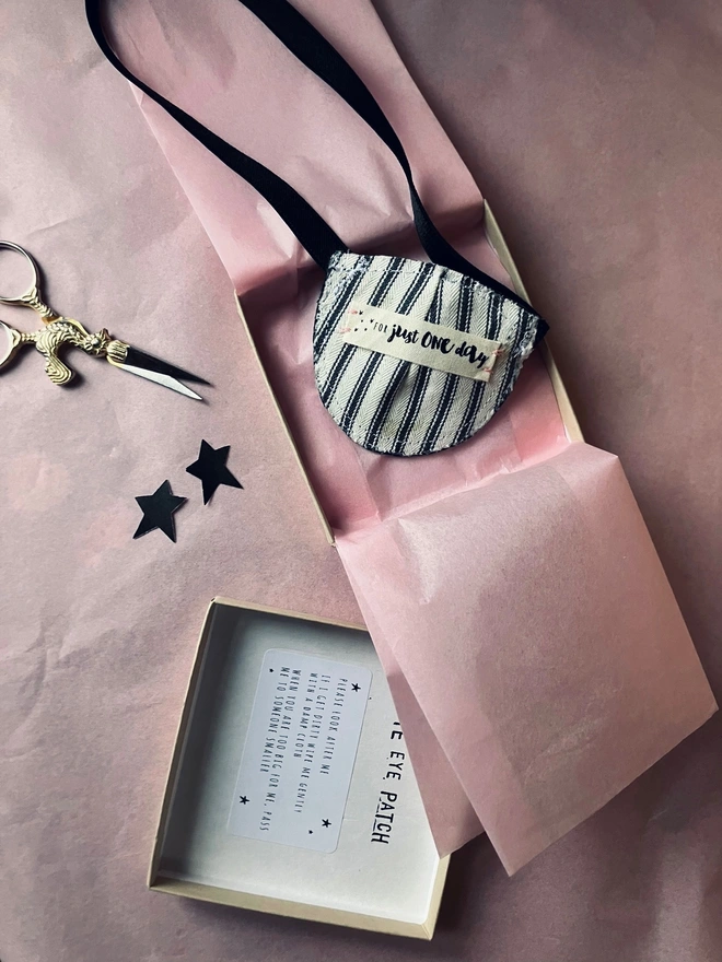 Eye patch on pink tissue placed in box, ticking stripe lining