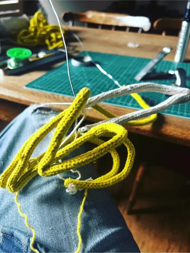 A partly made string and wire peeled banana tree topper resting on makers knee with tools on an oak table