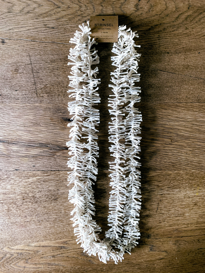 2 metre length of white Plain Cotton Strinsel (plastic free string tinsel) on an oak background