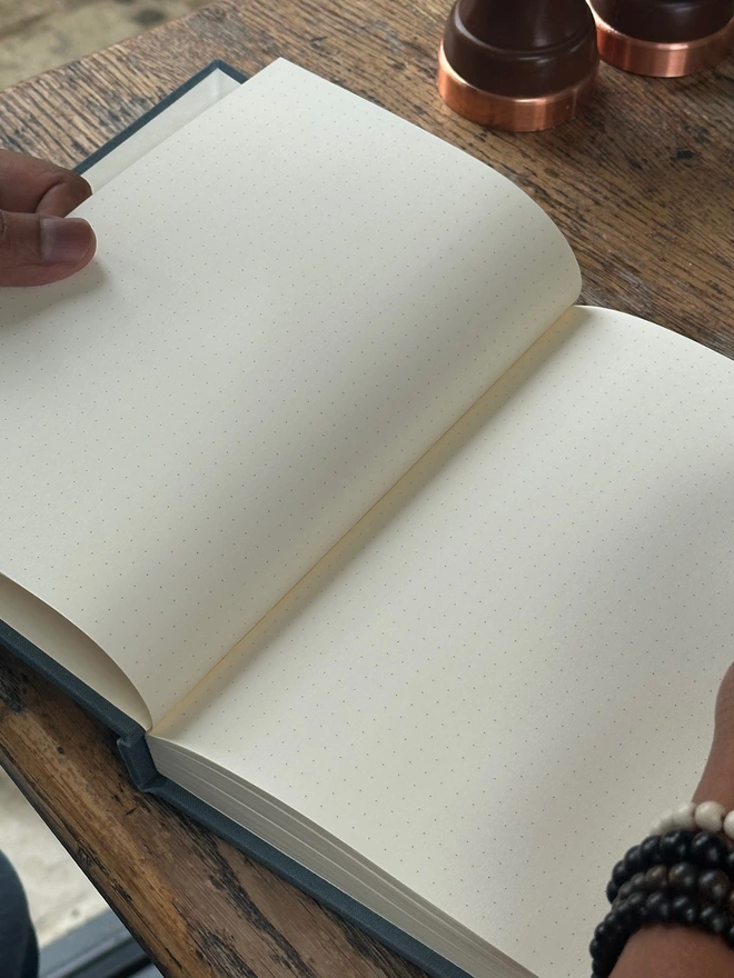 An open notebook filled with dotted bullet journal pages is held in a man's hands above a wooden table.