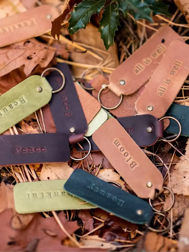 custom leather embossed keyring. a selection of green and brown leather keyrings photographed among fallen autumn leaves.