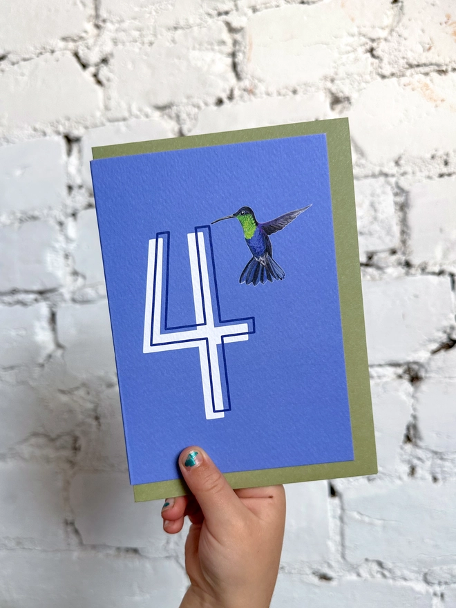 a deep purpley blue card with a big white number 4 and a hummingbird illustration and a green envelope