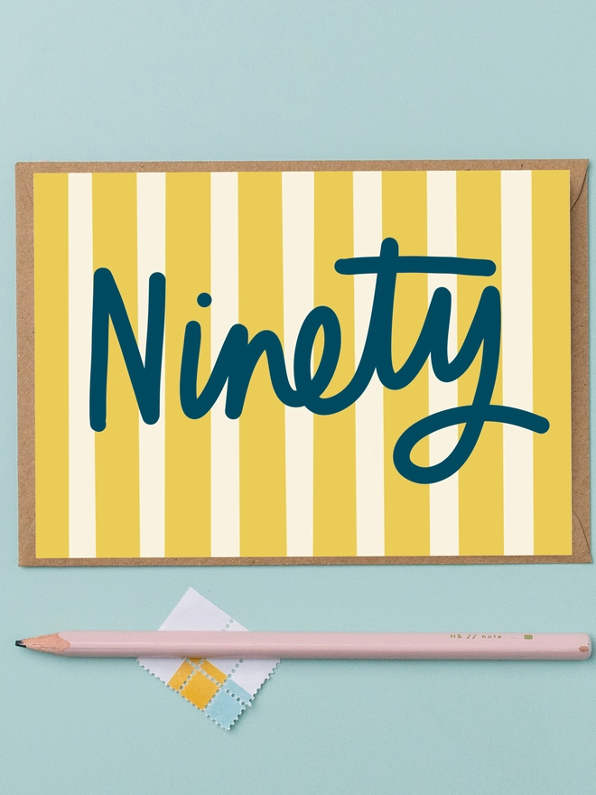 A 90th birthday card featuring the word ninety in navy lettering on a yellow and cream striped background 