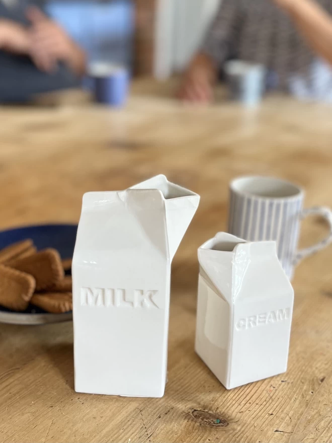 A handmade ceramic carton has ‘cream’ recessed in capital letters, stand with matching milk carton.